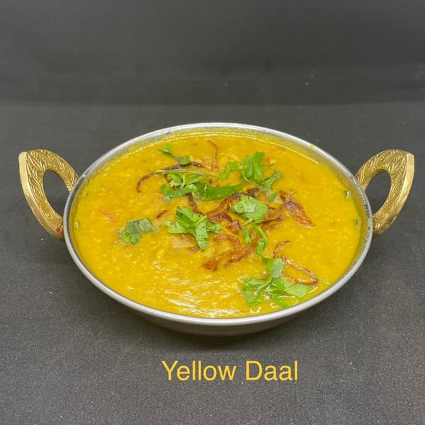 A golden yellow Jalsa Indian daal, garnished with fried onions and fresh cilantro, in a metal bowl.