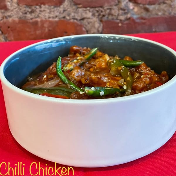 A bowl of Jalsa's Chilli Chicken, garnished with green chilies, on a red tablecloth.
