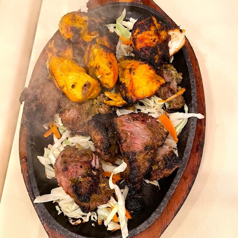 Sizzling Jalsa Indian platter with chicken tikka, lamb, and vegetables on a hot plate.