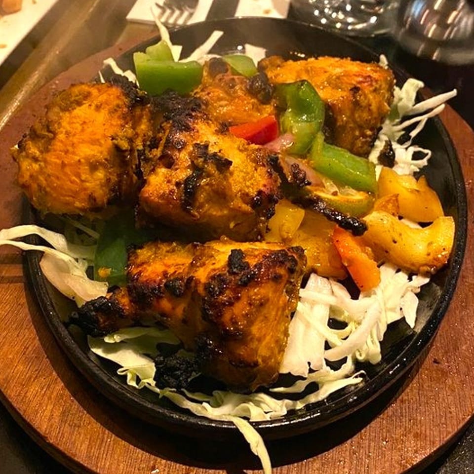Sizzling Jalsa chicken tikka with bell peppers and onions on a bed of shredded cabbage.